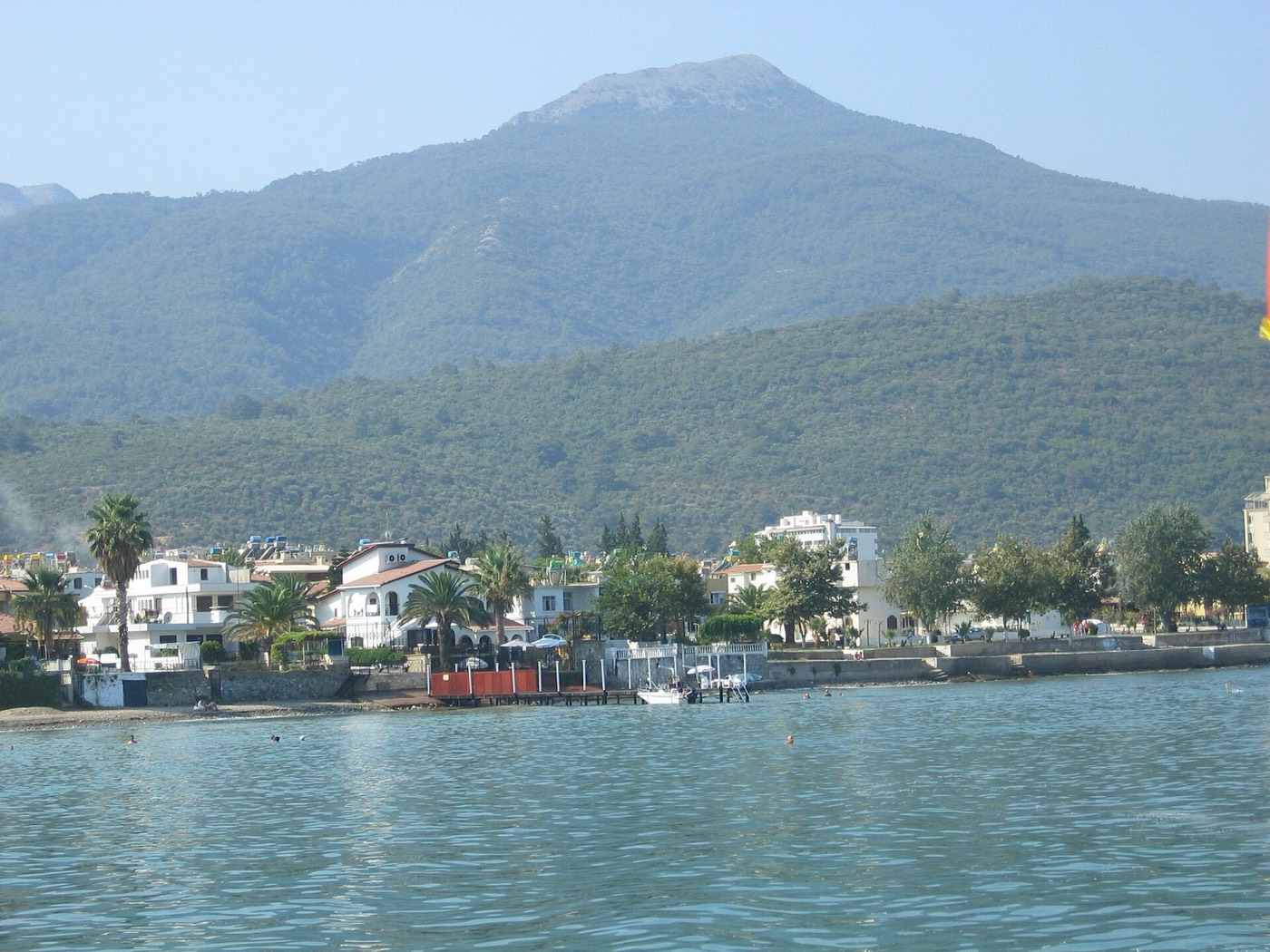 Denizden görülen Güzelçamlı kıyısı, palmiyeli evler ve arkada ormanlık dağ