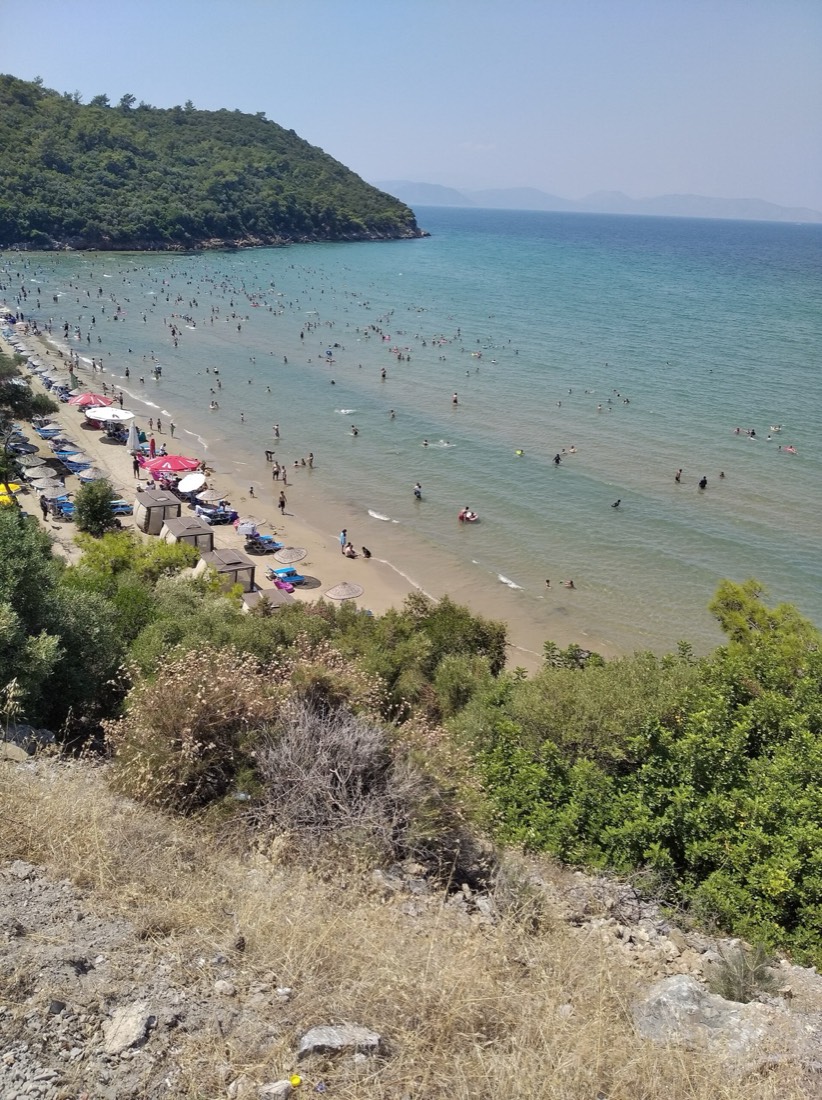 Yeşil tepeden görülen, şemsiyeli kumsal ve turkuaz deniz